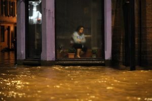 A woman sits inside a Chinese Restaurant watching floodwater race by the window in Dumfries, southern Scotland, on December 30, 2015 after heavy rainfall brought by Storm Frank.