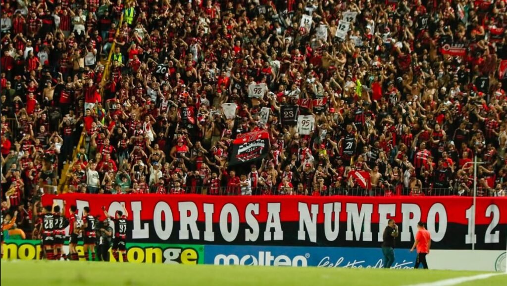 Afición de Alajuelense animando en las gradas del Estadio Alejandro Morera Soto con banderas y cánticos.