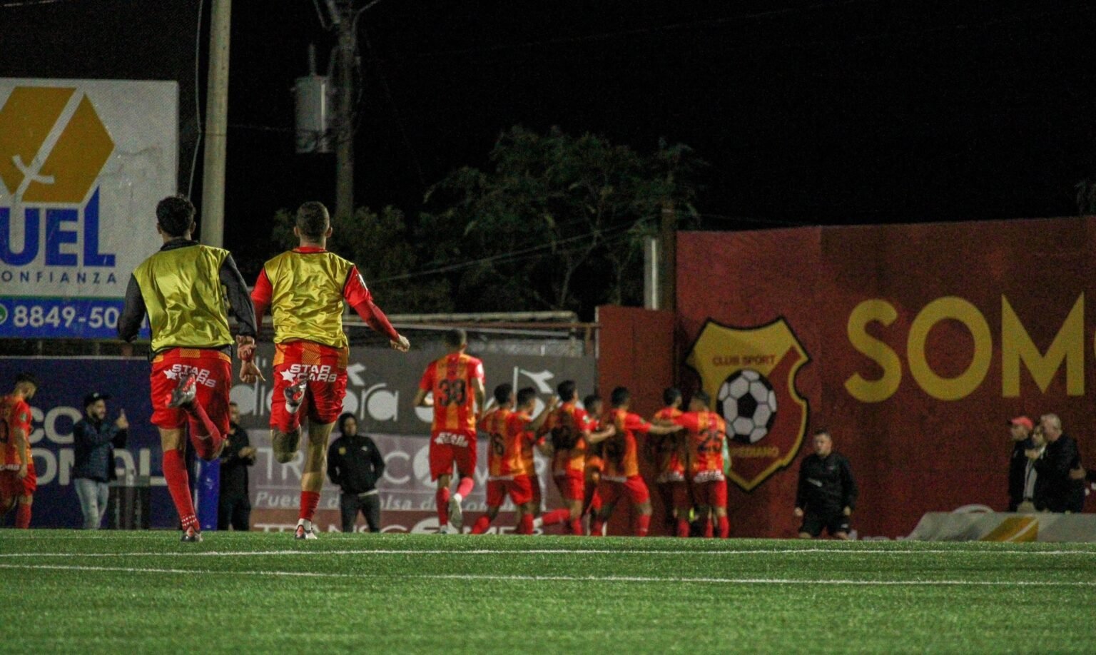 Jugadores del Club Sport Herediano corren hacia sus compañeros para celebrar un gol durante un partido nocturno en el Estadio Carlos Alvarado.