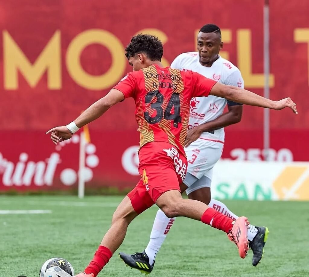 Jugador del Herediano, Andy Rojas, controlando el balón en un partido de fútbol mientras es marcado por un defensor del equipo rival